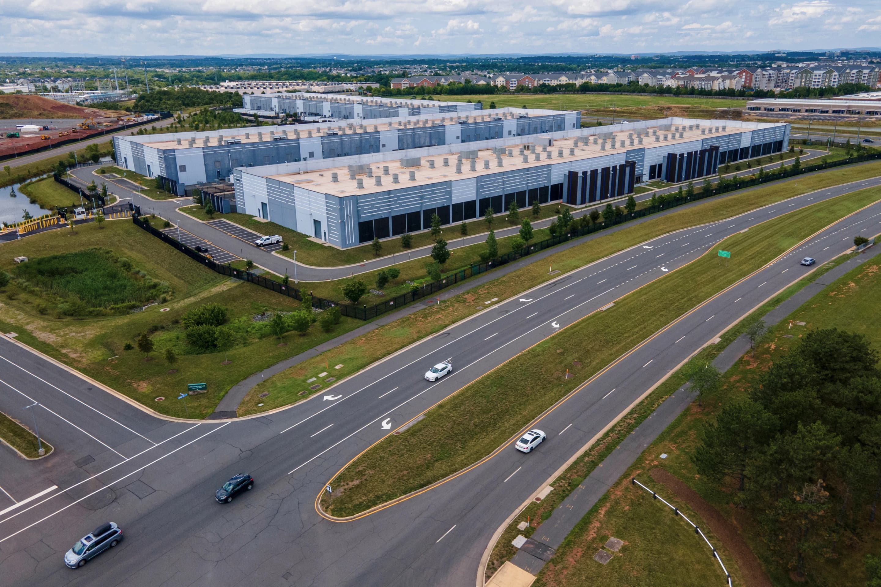 An aerial view of large AI data center warehouse buildings surrounded by roads and construction.
