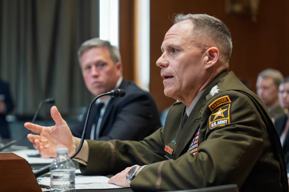 A U.S. Army general in uniform gesturing while testifying at a Senate committee hearing, with Defense Secretary Pete Hegseth seated behind him.