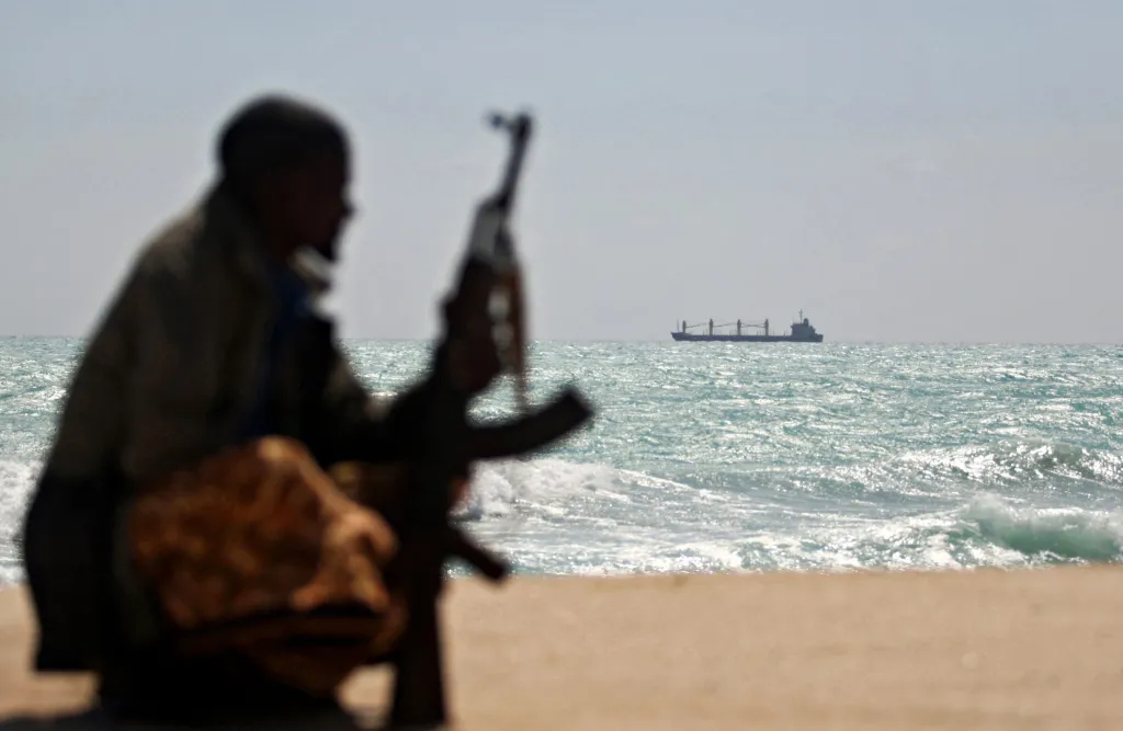 A pirate holding a rifle stands on a beach as a commercial tanker passes in the Gulf of Aden.