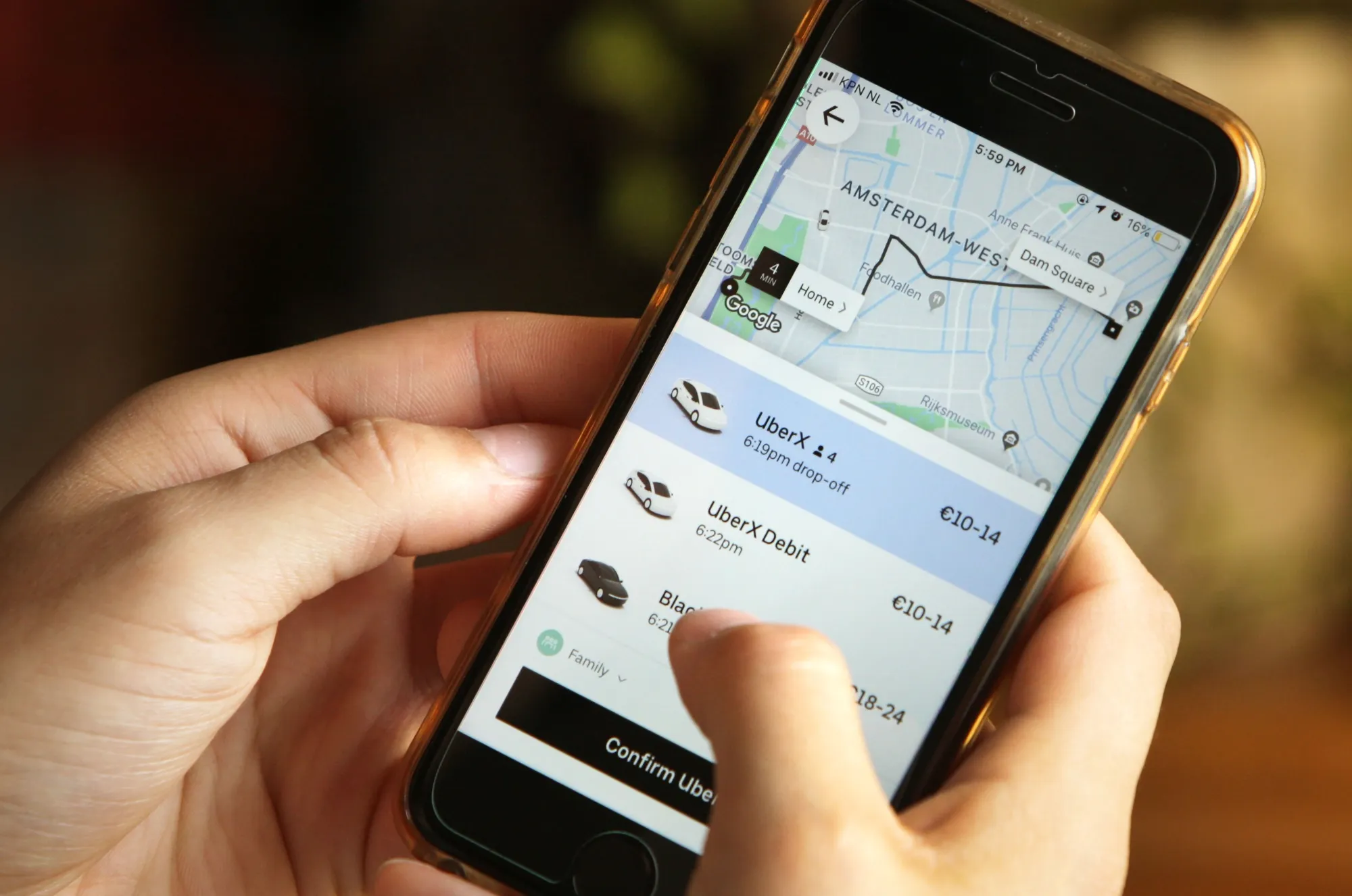 A person holding a smartphone displaying the Uber app with a map of Amsterdam and ride options.