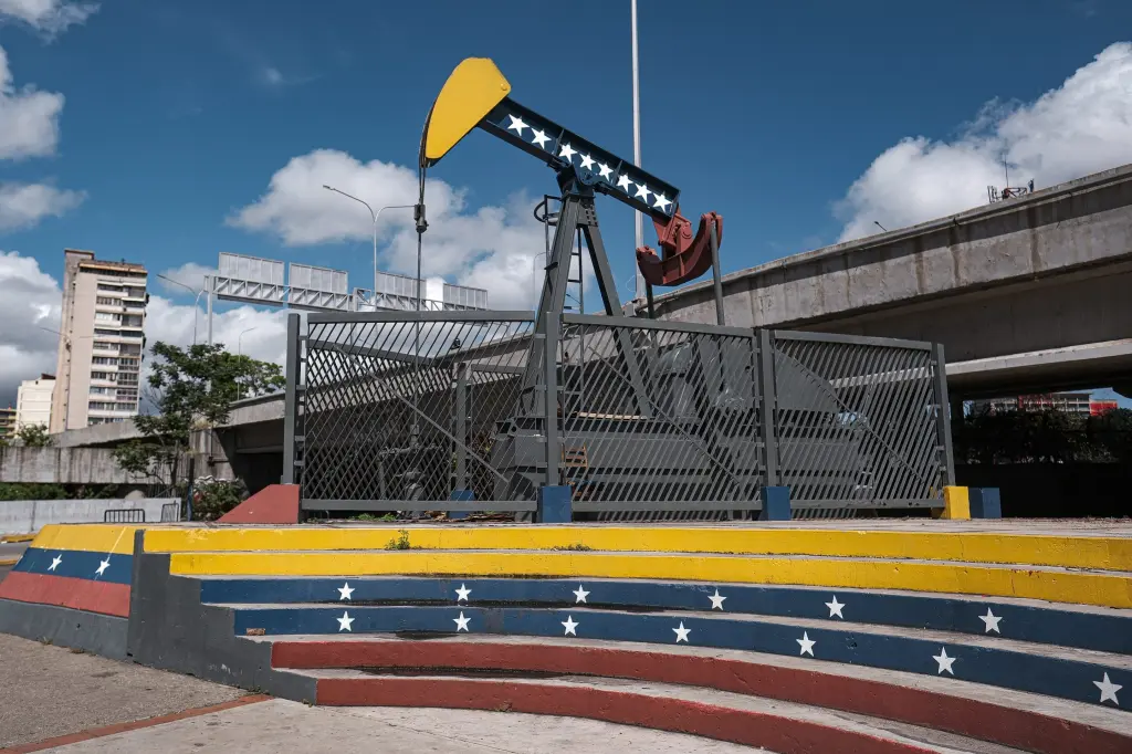 An oil pump jack behind a fence painted with the colors of the Venezuelan flag in Caracas.