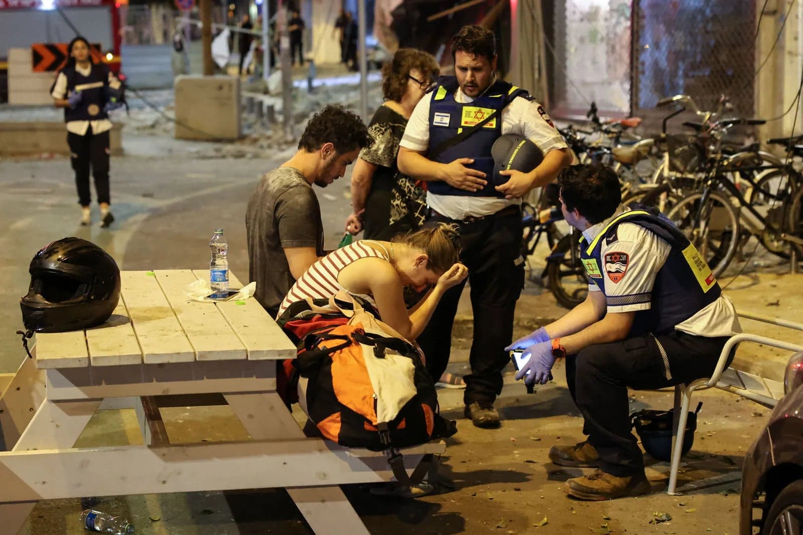 First responders comforting a woman at a picnic table after a rocket strike in Tel Aviv