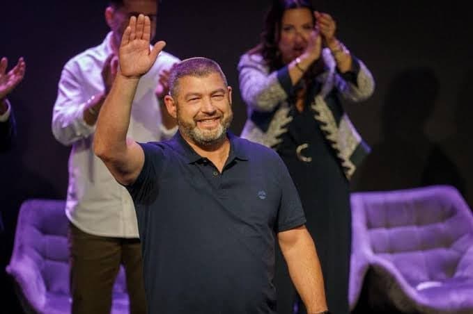 Ofer Winter waving to a crowd on stage with people applauding behind him