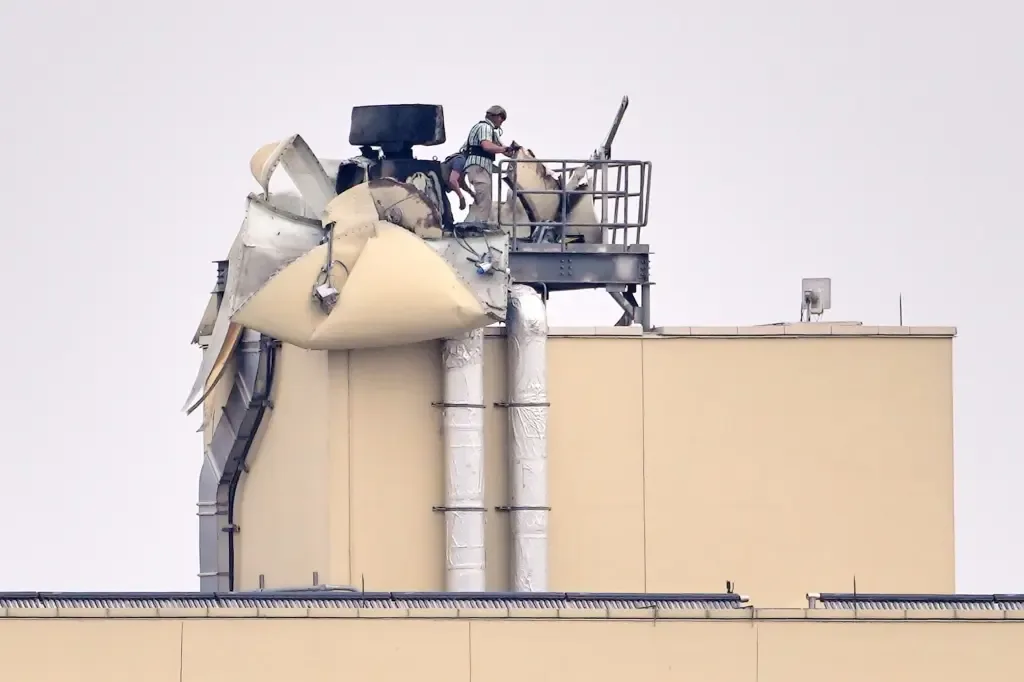 A damaged rooftop structure at a U.S. military facility with a worker inspecting the wreckage