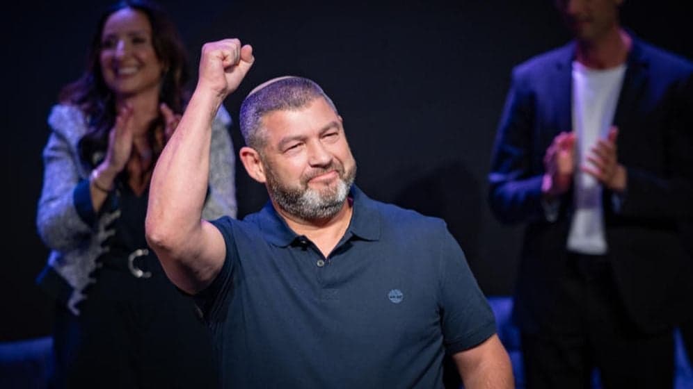 Ofer Winter raising his fist in celebration on stage with supporters clapping behind him