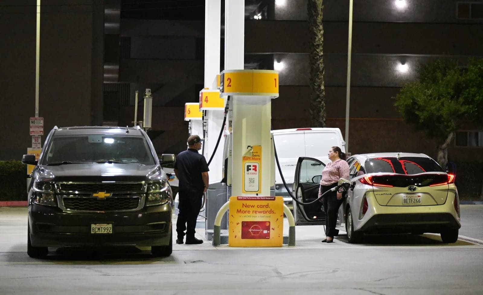 Two customers fueling their vehicles at a gas station pump at night