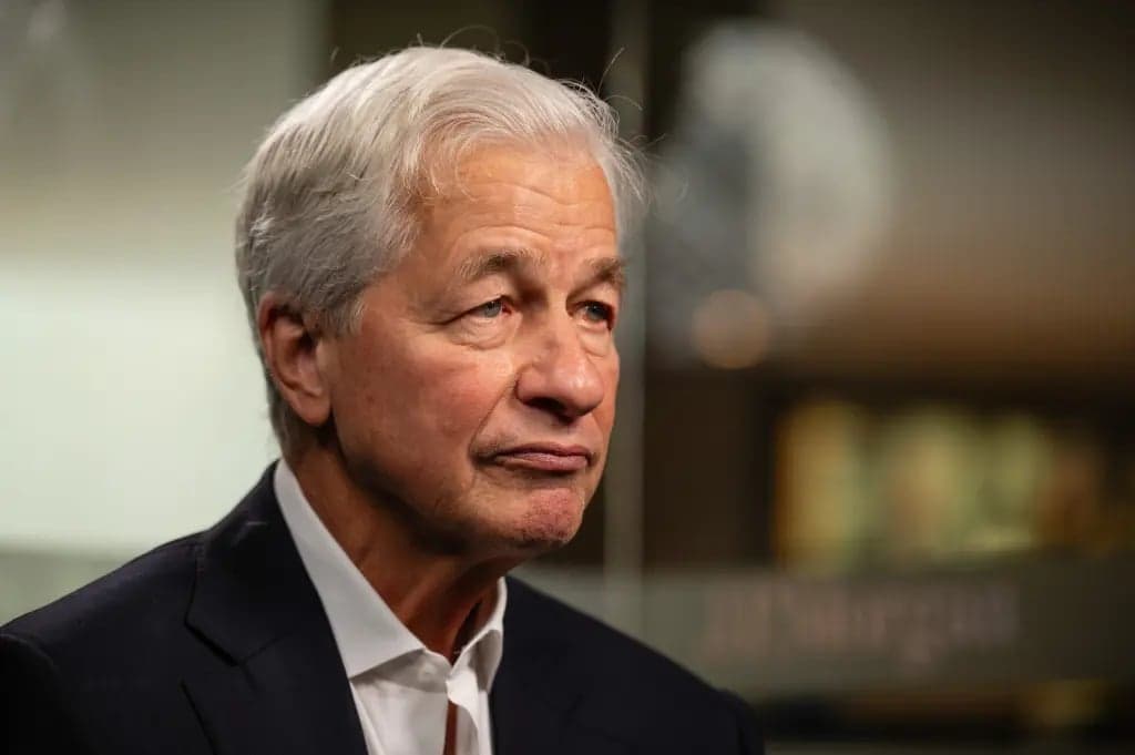 JPMorgan Chase CEO Jamie Dimon looking to the side indoors, with a blurred JPMorgan sign visible behind him